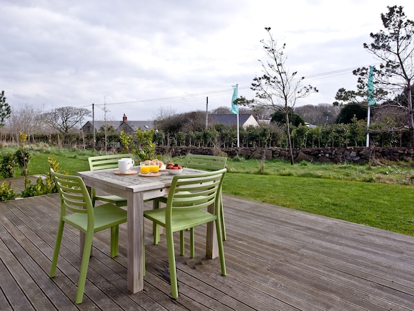 A wooden deck with a table and chairs, a bowl of strawberries, and a glass of orange juice.