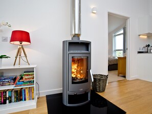 A modern living room with a wood-burning stove, a bookshelf with books, and a red lamp.