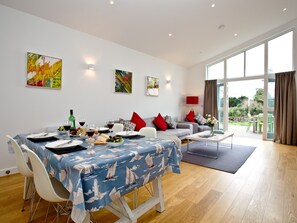 Un área de comedor con una mesa dispuesta para dos, un sofá con cojines rojos y un ventanal con cortinas.