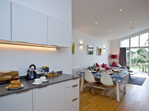 A modern kitchen with white cabinets, a dining area with a table and chairs, and a view of the outdoors. - Una Argentum 63 Carbis Bay (Carbis Bay, near St Ives)