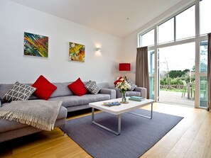 Una sala de estar moderna con un sofá gris, cojines rojos y blancos, una mesa de centro blanca y un jarrón con flores.
