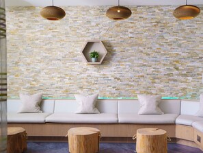 A modern interior with a stone mosaic wall, a beige sofa with cushions, and three wooden stools. - Una Argentum 63 Carbis Bay (Carbis Bay, near St Ives)
