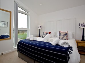A bedroom with a large window, a bed with white linens and a blue-striped blanket, two bedside lamps, and a wooden nightstand.