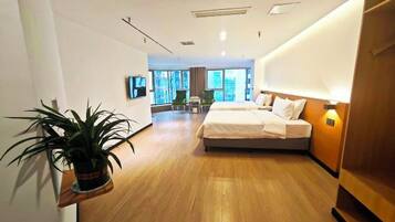 A hotel room with a bed, a potted plant, a TV, and a view of the city.