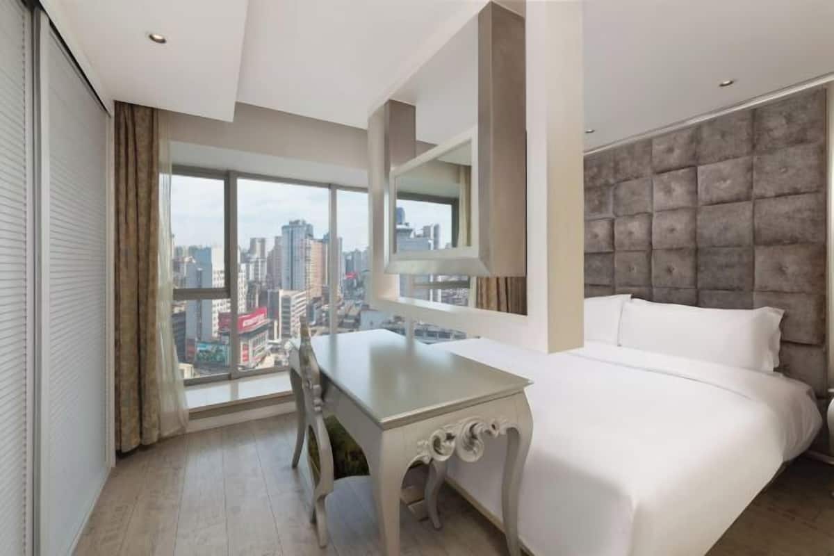 Een moderne hotelkamer met een groot bed, een bureau en uitzicht op een stadsgezicht.
