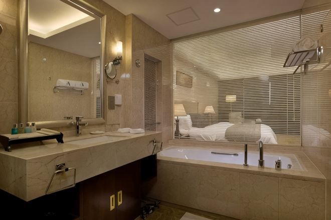 A modern bathroom with a large mirror, a bathtub, and a vanity with toiletries.