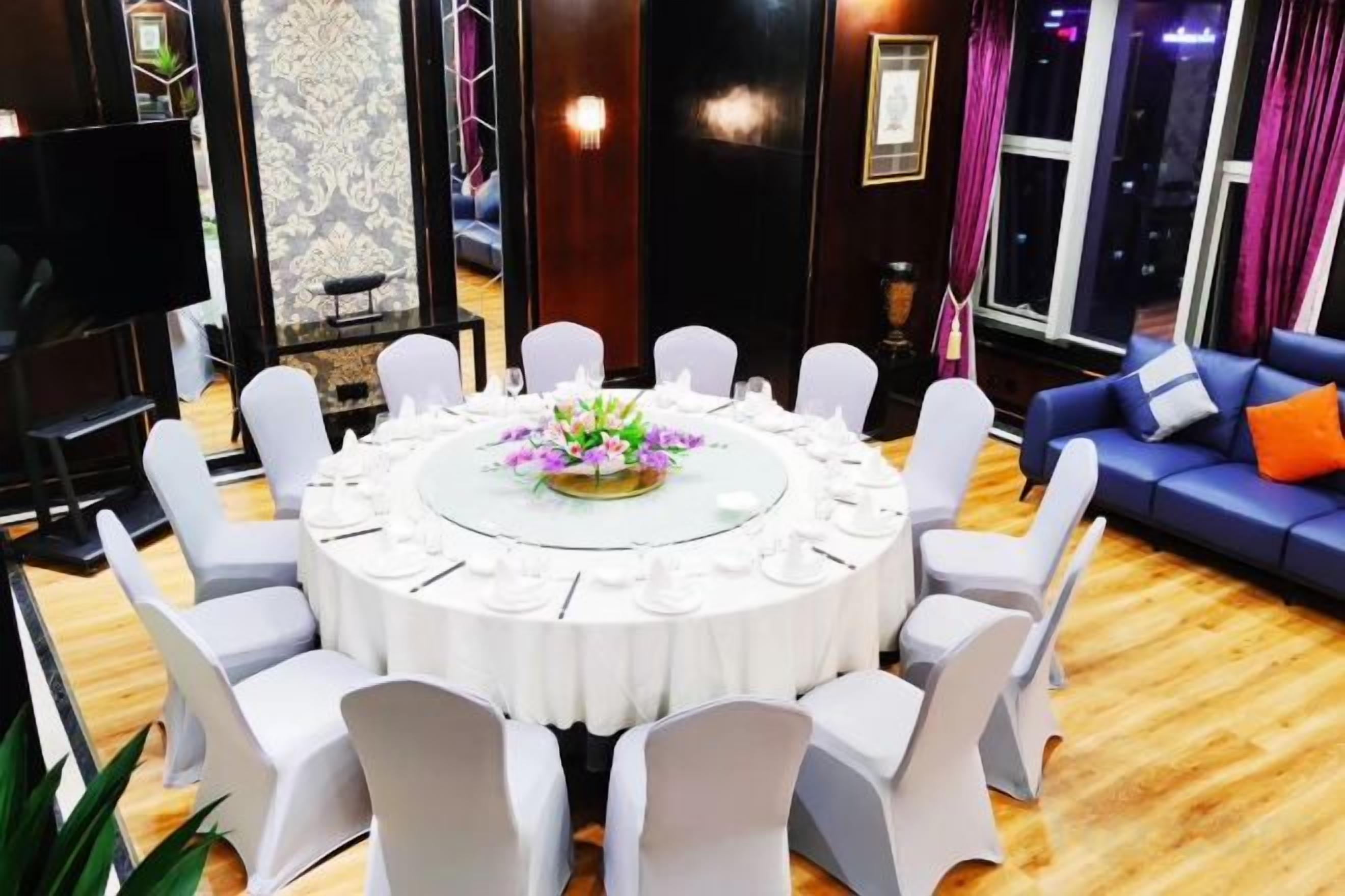 A round table with white chairs, a floral centerpiece, and a TV in the background.