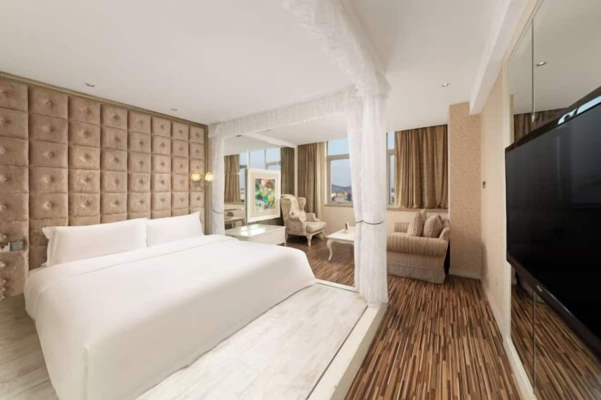 Een hotelkamer met een groot bed, een televisie, een zithoek met een bank en fauteuils, en uitzicht op de omgeving.