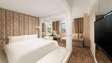 A hotel room with a large bed, a TV, a seating area with a sofa and armchairs, and a view of the outdoors.