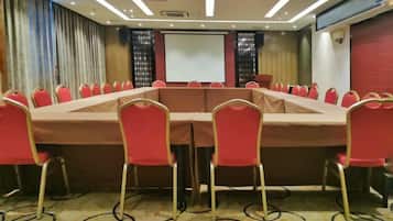 A conference room with a long table, red chairs, and a projector screen.