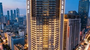 Een hoog gebouw met verlichte ramen, omringd door andere hoge gebouwen in een stadsgezicht.