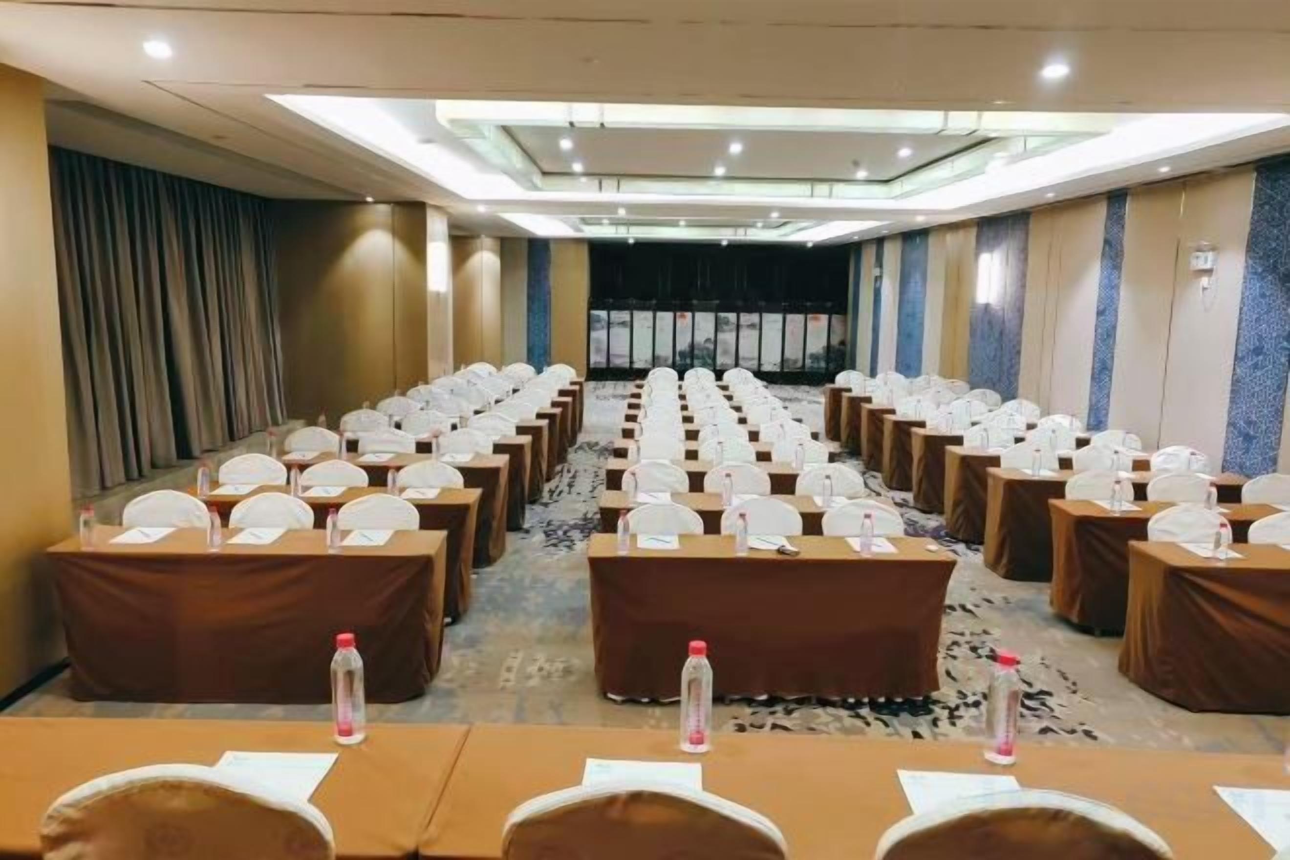 Un salón de conferencias con filas de mesas, sillas y tarjetas de identificación, equipado con botellas de agua.