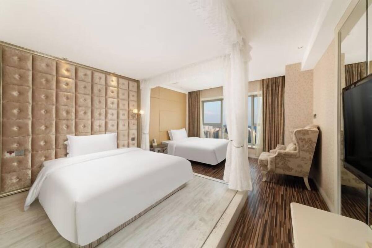 Een hotelkamer met twee bedden, een groot paneel aan de wand, een televisie en een raam.