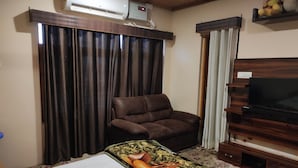 A hotel room with a bed, a brown leather chair, a television on a wooden stand, and an air conditioning unit on the wall. - Lajawab Homestay  (Srinagar)