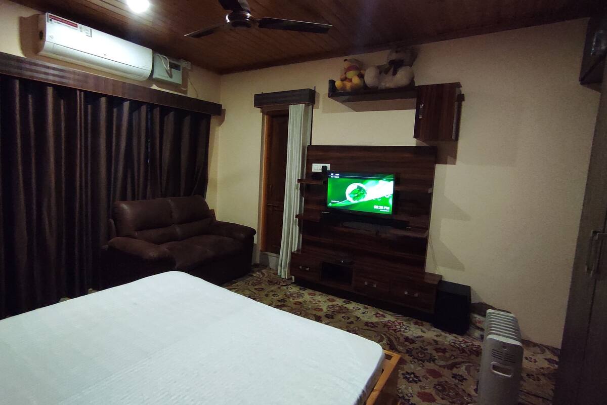 A room with a bed, a brown leather chair, a television on a wooden stand, and a ceiling fan.