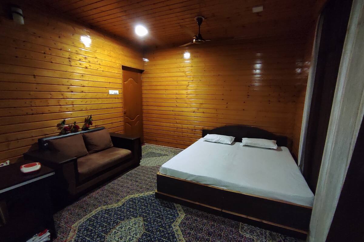 A wooden-paneled room with a bed, a sofa, and a nightstand.