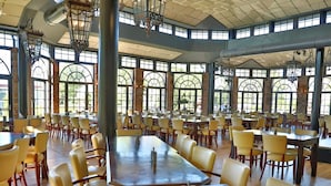 Uma ampla sala de jantar com pé direito alto, janelas grandes e lustres tradicionais.