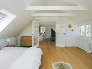A bedroom with a sloped ceiling, wooden flooring, a bed, a dresser, a door leading to a staircase, and a radiator.
