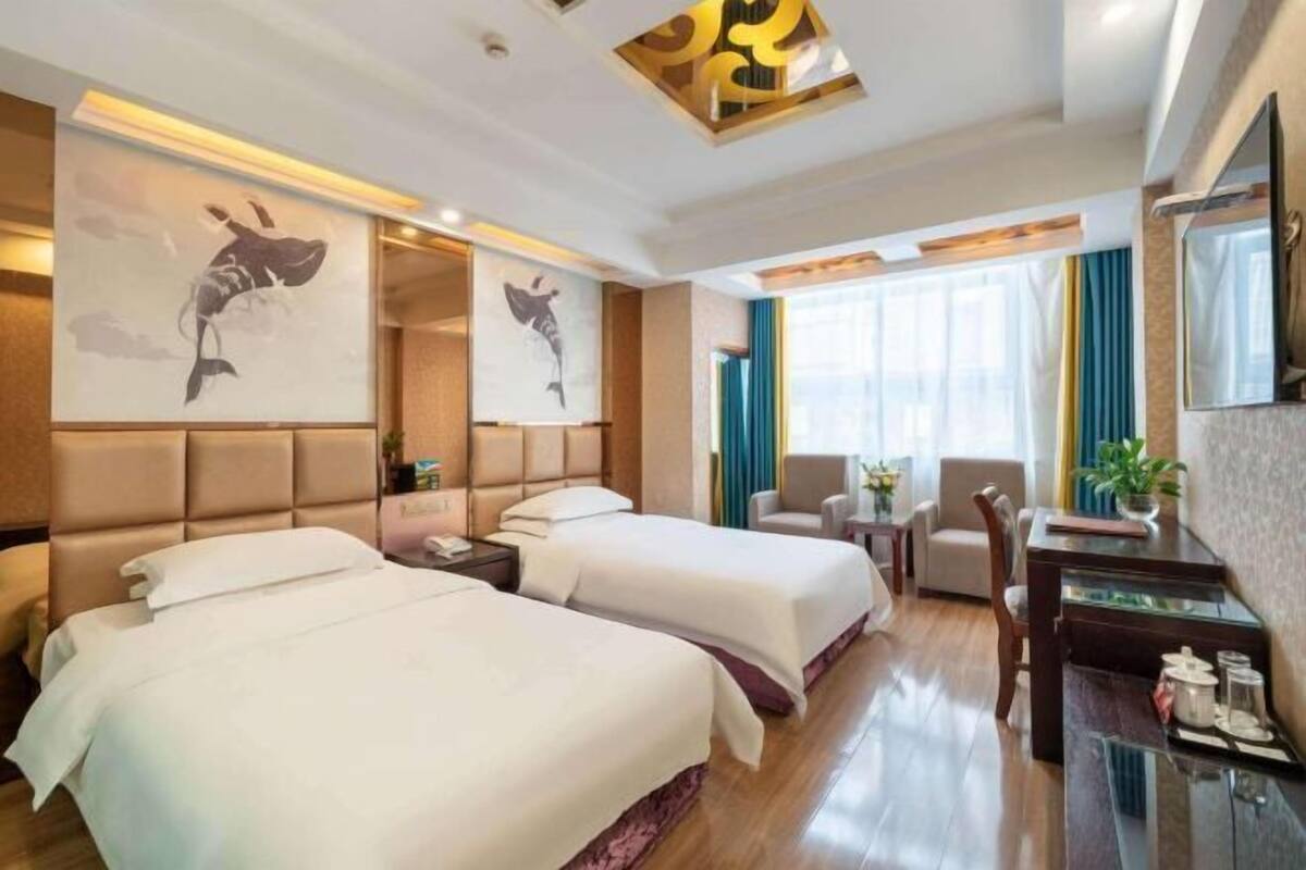 A hotel room with two beds, a desk, a chair, a TV, and artwork on the walls.