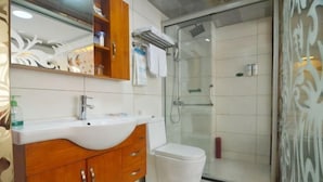 A bathroom with a white sink, wooden vanity, a toilet, and a glass shower enclosure.