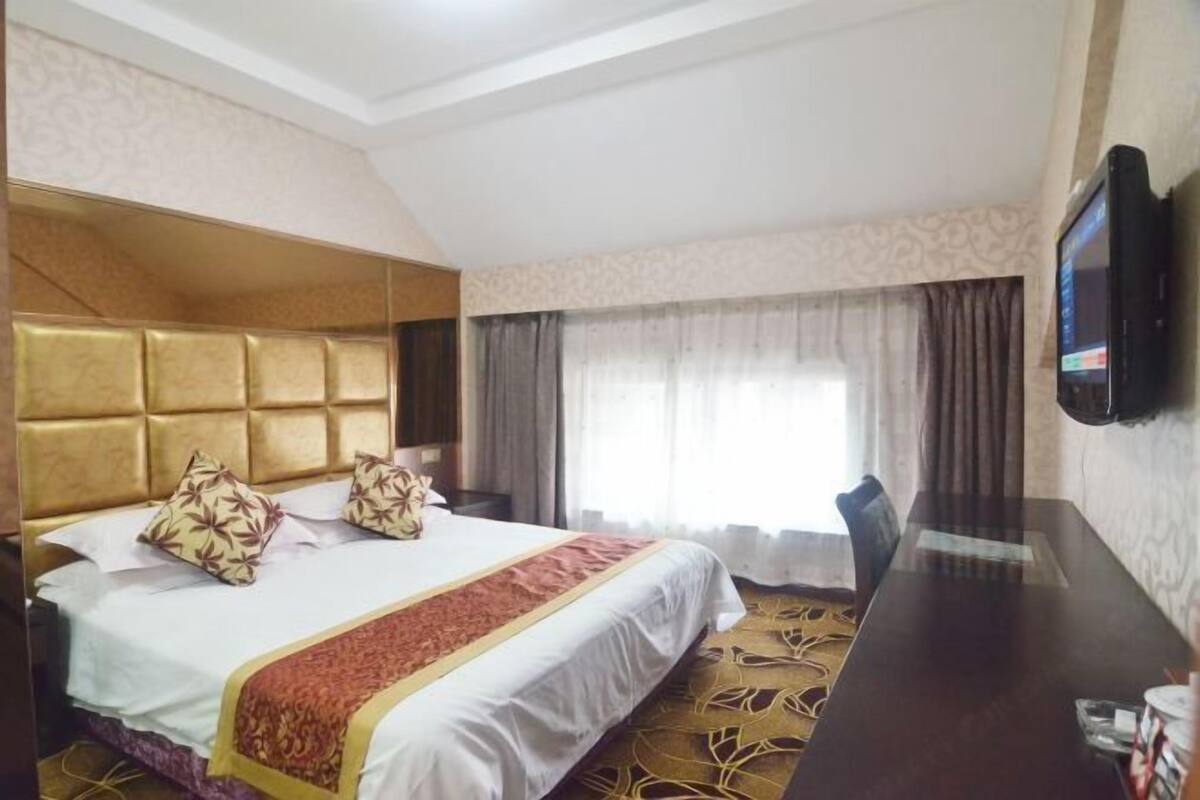 A hotel room with a large bed, a flat-screen TV mounted on the wall, a desk, and a window with curtains.
