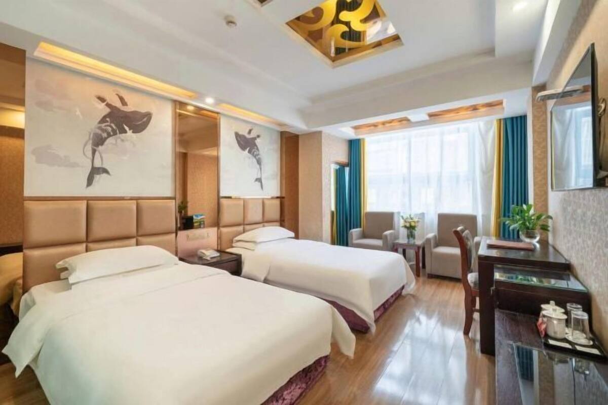 A hotel room with two beds, a desk, a chair, a TV, and artwork on the walls.