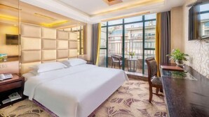 A hotel room with a large bed, a desk, a chair, and a balcony with a view.