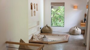 Un interior minimalista con una hamaca, sillones de plumas y vistas a la vegetación a través de una ventana.