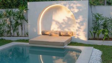 A modern outdoor seating area with a pool, surrounded by greenery and a white wall.