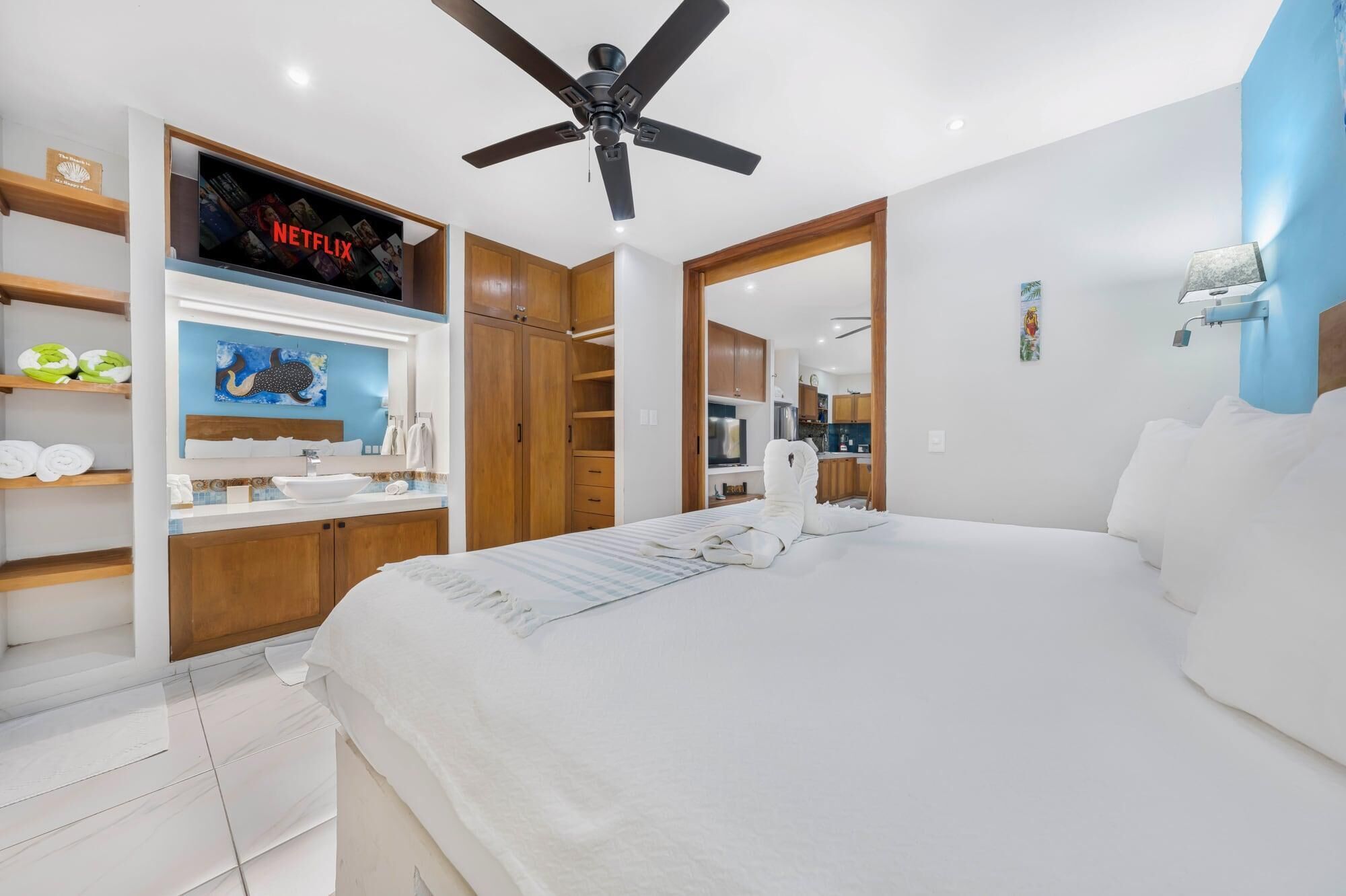 A hotel room with a bed, a TV displaying Netflix, a ceiling fan, and a bathroom with a shower and sink.