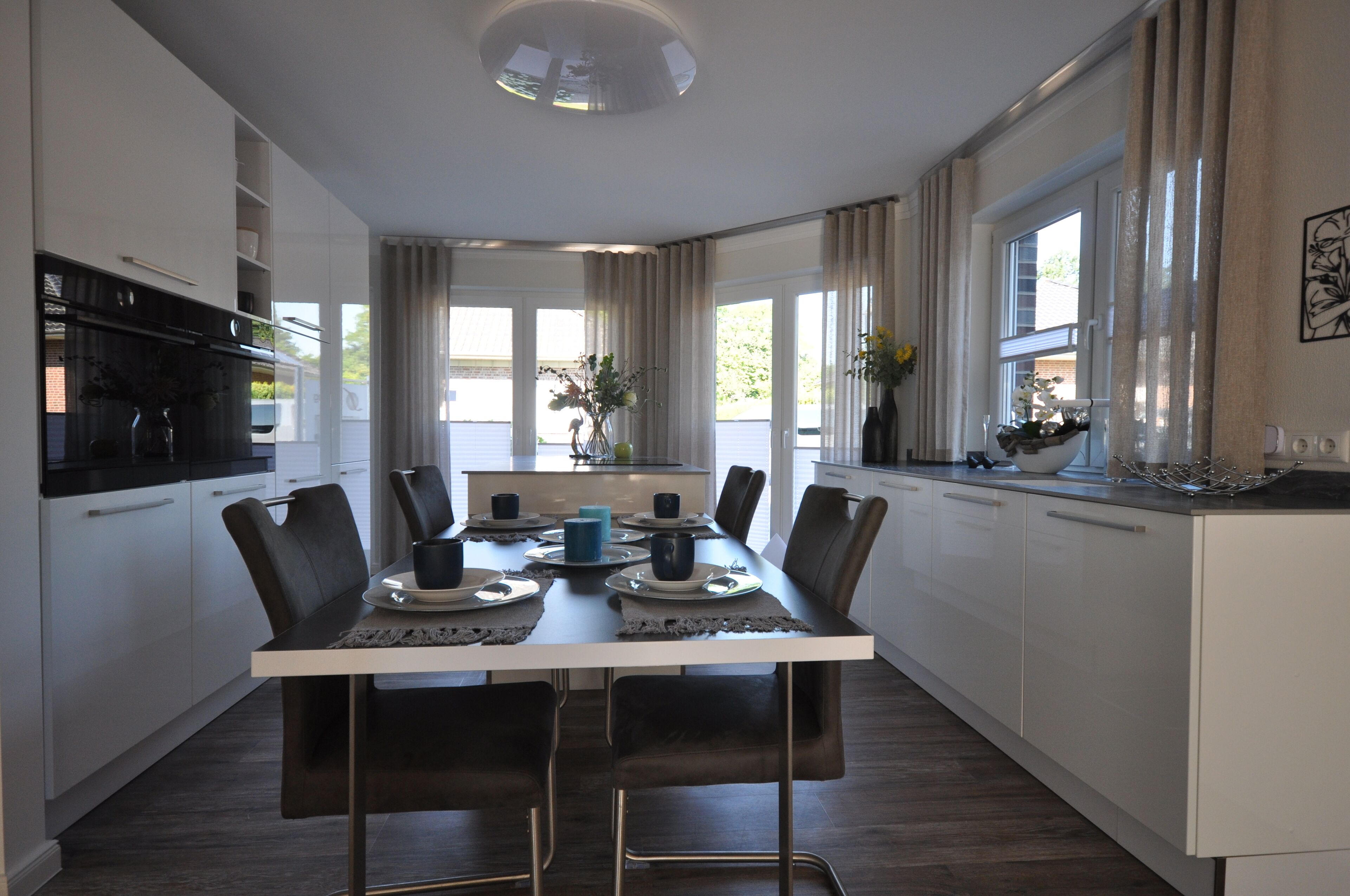 Une cuisine moderne avec des meubles blancs, un réfrigérateur noir et une table à manger pour six personnes, accompagnée de chaises.