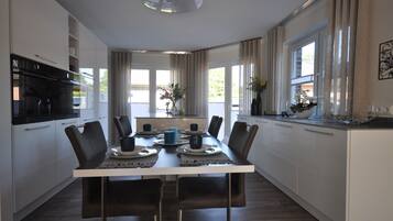 Une cuisine moderne avec des meubles blancs, un réfrigérateur noir et une table à manger pour six personnes, accompagnée de chaises.