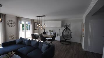 A modern living room with a dark blue sofa, a dining area with a table and chairs, and a hanging chair.