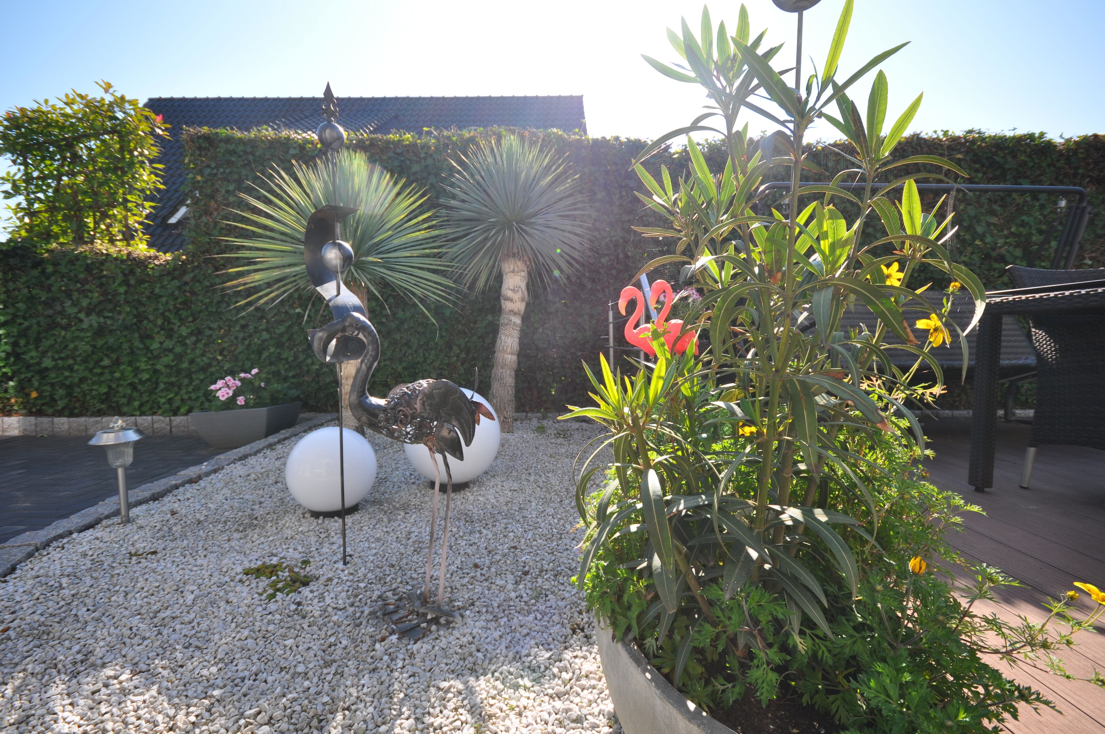 A garden with a sculpture of a bird, a palm tree, and a planter with yellow flowers.