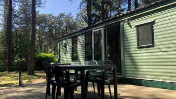 A green mobile home with a deck, two chairs, and a table.
