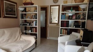 Een woonkamer met een bank, een witte fauteuil en twee boekenkasten vol boeken en decoratieve objecten.