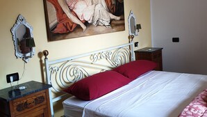Een slaapkamer met een bed, nachtkastje, dressoir, schilderij aan de muur en een spiegel.