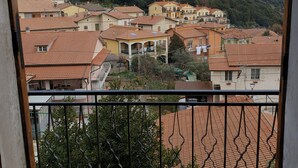 Een balkon met uitzicht op een woongebied met terracottadakpannen en een heuvel op de achtergrond.