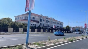 A multi-story building with a red roof, a blue car on the road, and a clear blue sky. - Ziqi Hotel (Shanghai Bay University Town) (Shanghai)
