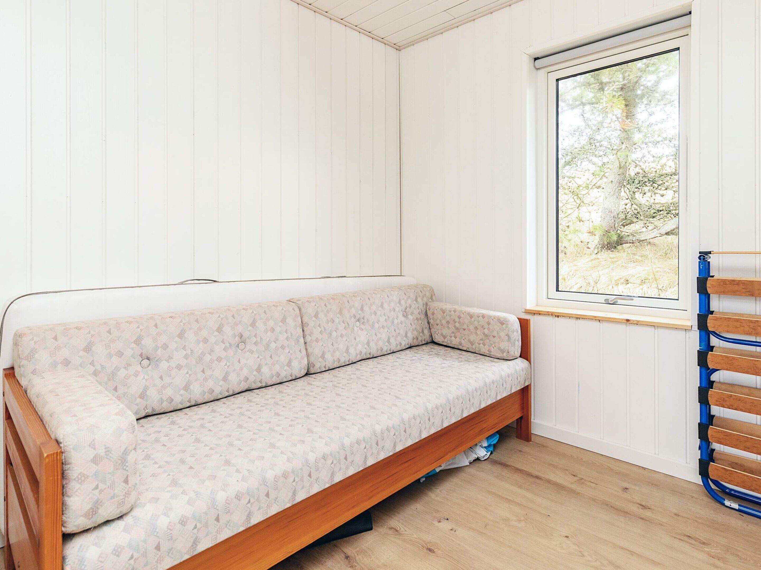 A room with a wooden floor, a white paneled wall, a window with a view of trees, and a wooden bench.
