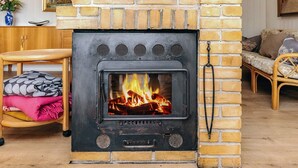 A fireplace with a visible fire, a wooden bench, a chair, and a sofa in a room with a brick wall. - 4 Star Holiday Home in Pandrup (Pandrup)
