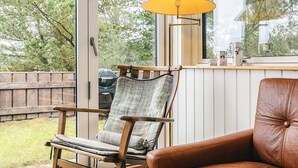 A room with a wooden chair and a brown leather sofa, a lamp, and a view of the outdoors. - 4 Star Holiday Home in Pandrup (Pandrup)