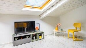 A modern living room with a skylight, a flat-screen TV, a minimalist coffee table, a yellow chair, and a small cabinet with decorative items. - Sloping Roof in the center of Naples (Napoli)