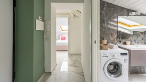 A modern bathroom with a marble floor, a built-in washing machine, and a large mirror above the sink. - Sloping Roof in the center of Naples (Napoli)
