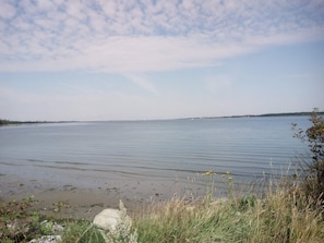 A calm lake with a clear sky, surrounded by grassy areas and some rocks. - 6 Person Holiday Home in Storvorde (Storvorde)