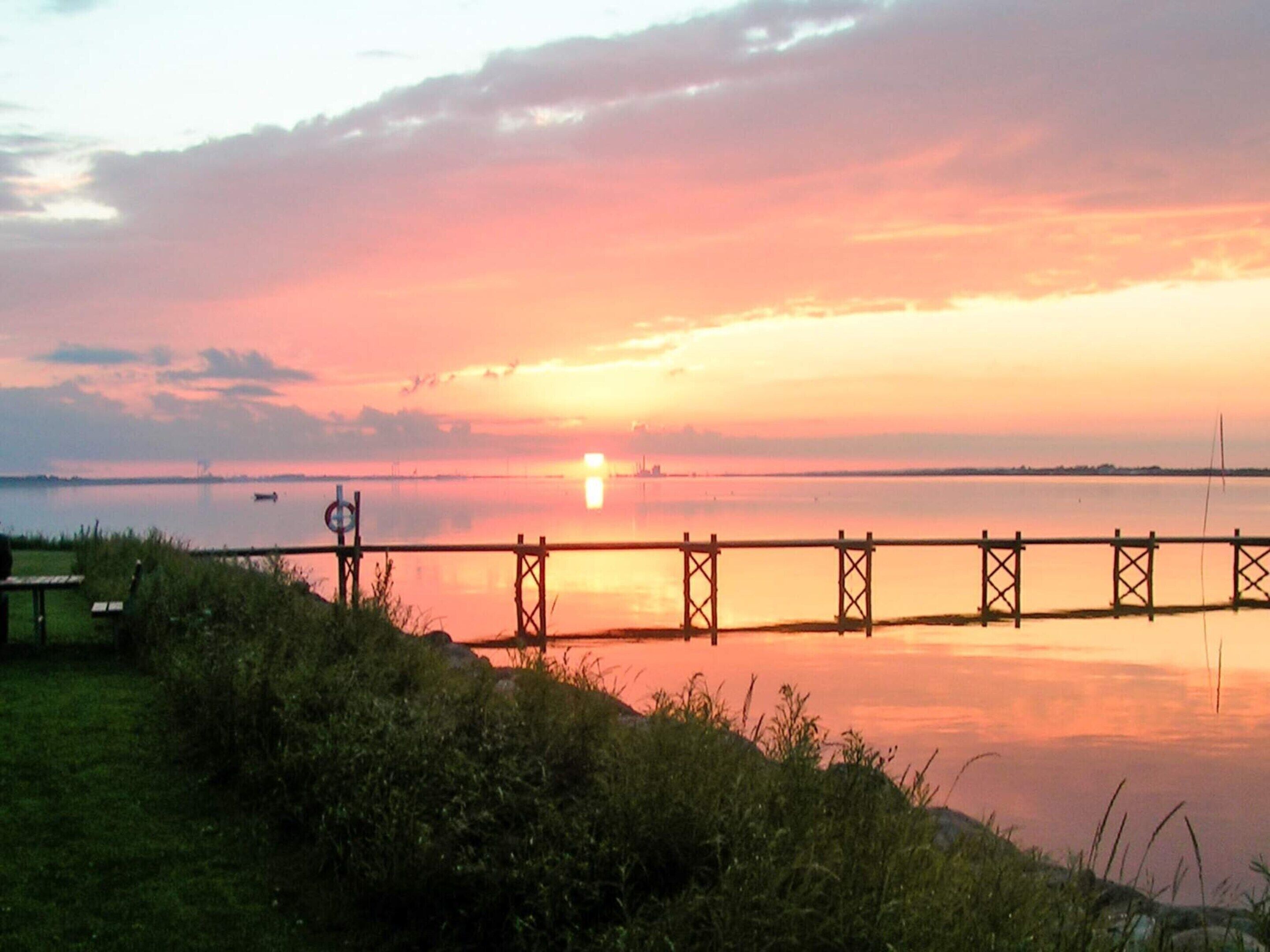 A sunset over a calm body of water with a dock extending into the water.