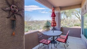 Une terrasse extérieure avec une table ronde et des chaises, un parasol rouge et une sculpture décorative en forme de soleil fixée au mur.