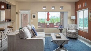 Un salon comprenant un canapé, un fauteuil, une table basse et donnant sur l’extérieur grâce à une porte coulissante.