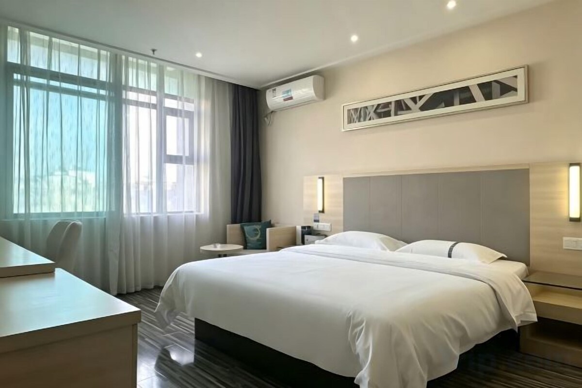A hotel room with a large bed, bedside tables, a desk, and a window with curtains.
