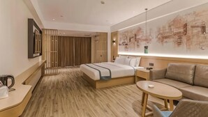 Une chambre d’hôtel comprenant un lit, un canapé, une petite table, une table de chevet et un téléviseur fixé au mur.